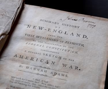 Detail of a printed book shows title page with manuscript notations at the top of the page.