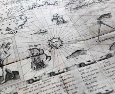 Detail of a printed map shows decorative elements such a sun, a person carrying arrows, ships and fish at sea, a scale, and a key with text in French at the bottom of the map.