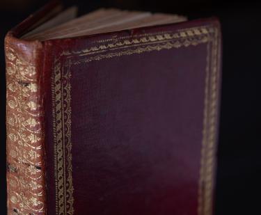 Detail of a printed book shows red binding with gold details at the borders of the boards and all along the spine.