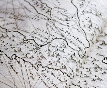 Detail of a printed map shows text in French, latitude and longitude lines, and small mountains.