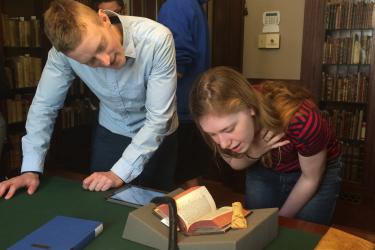two people standing over a table looking at a rare book