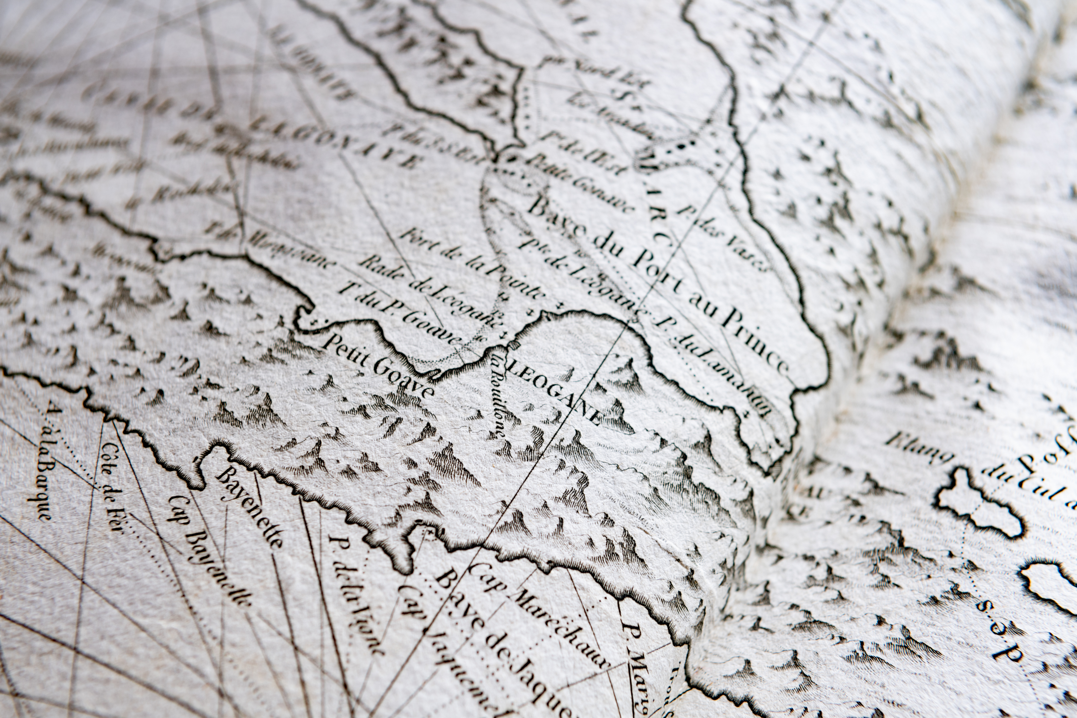 Detail of a printed map shows text in French, latitude and longitude lines, and small mountains.