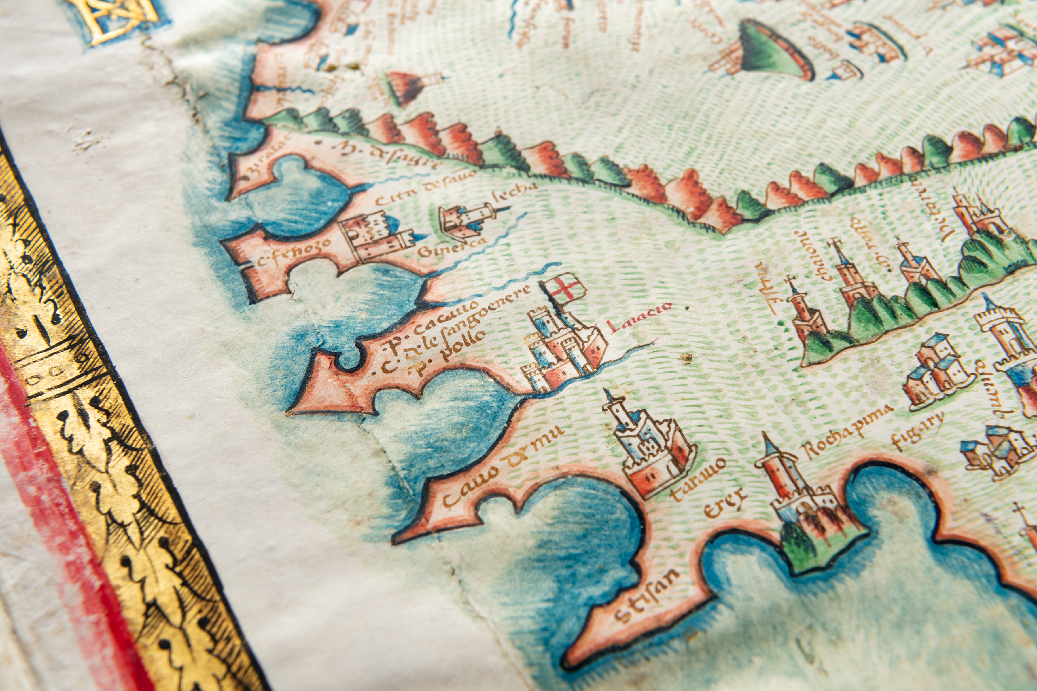 Detail of a colored manuscript atlas shows a coastal region and labels in Latin. Other details include drawings of castles and mountains.