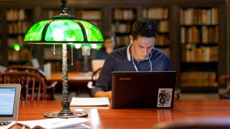 man seated at a table in front of a laptop and green lamp