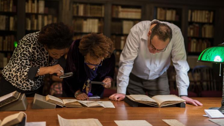 group of people standing around a table looking down at several books