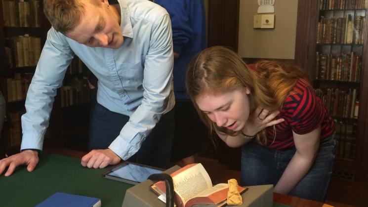 two people standing over a table looking at a rare book