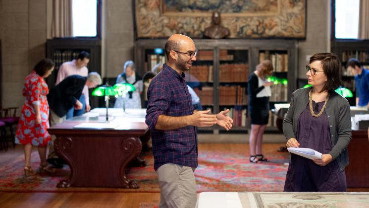 Ernesto Bassi and Bertie Mandelblatt discuss a map while researchers consult maps and books in the background