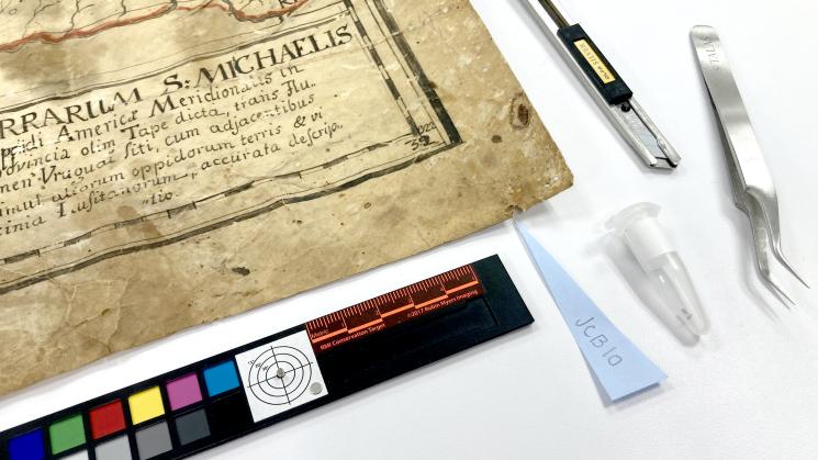 The image shows a yelowed document and conservation tools.