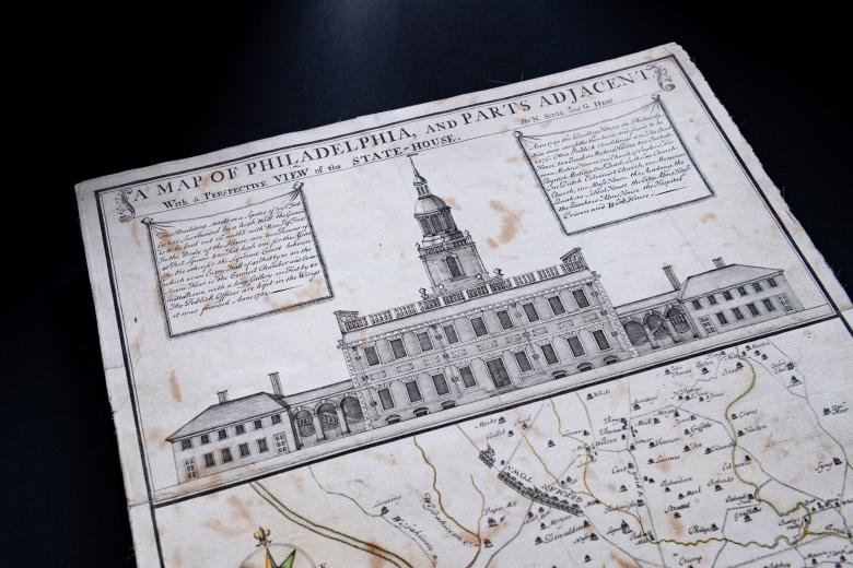 Detail of hand colored, engraved map of Philadelphia, Pennsylvania shows prospective view of the State House. Text in English shows the title of the map "Map of Philadelphia, and parts adjacent. With a prospective view of the State-House." Other text in English describing the building is out of focus.