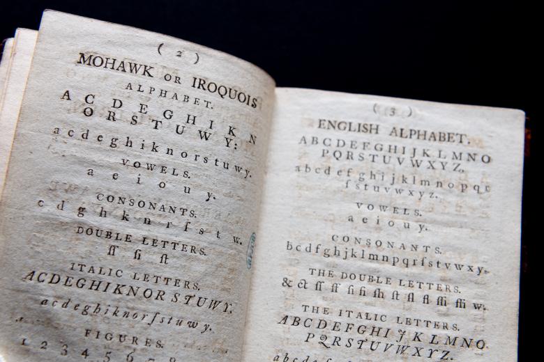 Detail of a printed book shows a page dedicated to writing out the Mohawk alphabet and the opposite page shows the English alphabet.