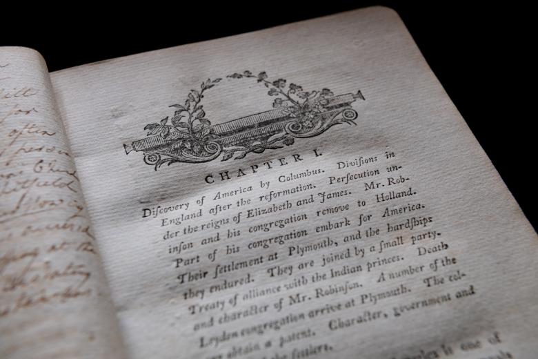 Detail of a printed book shows page with text in English reading "Chapter I" at the top. Also includes a small decorative illustration.