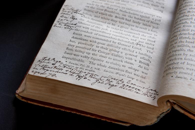 Detail of a printed book shows a page with text in English and manuscript notations at the bottom and side margins.