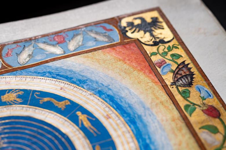 Detail of a colored manuscript map shows cosmographical view of the world and zodiac. Inks in red, green, and blue and gilded details are used throughout the map and decorative border. Also visible are small heads in the gradient area.