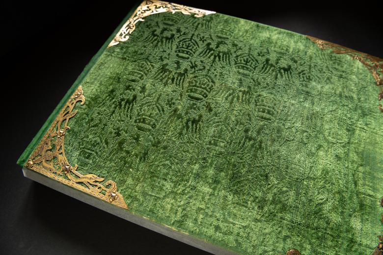 Detail of green velvet book binding shows pattern and gold corners on the front and rear boards.