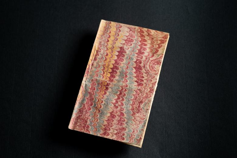 Detail from book cover shows marbled paper in red, yellow, and blue tones.