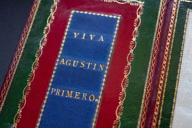 Printed book bound in red and green Morocco and blue silk with text in Spanish reading "Viva Agustin Primero" on the inner front cover.