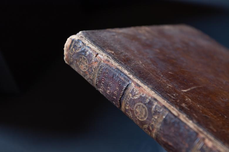 Detail of a red Morocco binding shows wear near the spine. Partial view of the title on the spine.