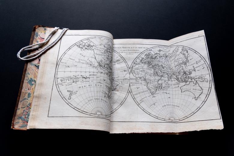 Detail of a printed book shows a fold-out map of the world. Some text in French is visible.