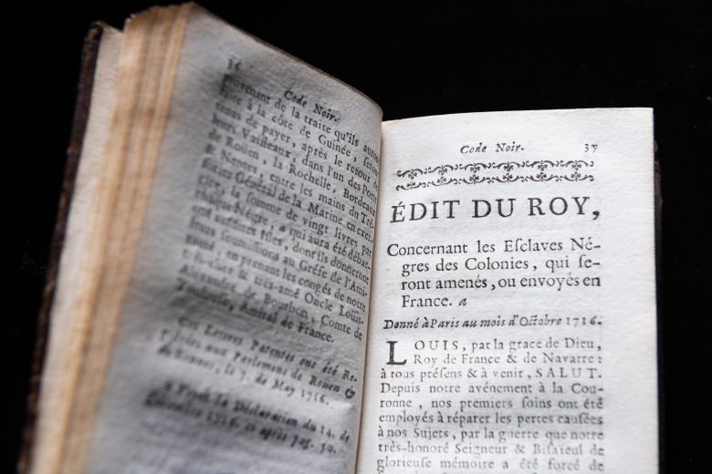 Detail of a printed book shows a page with text in French and decorative headpiece.