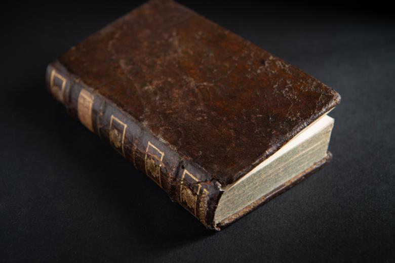 Printed book bound in brown leather shows decorative gilded elements on the spine.