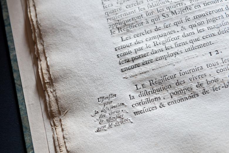 Detail of a printed book shows text in French and printed notes in the margins.