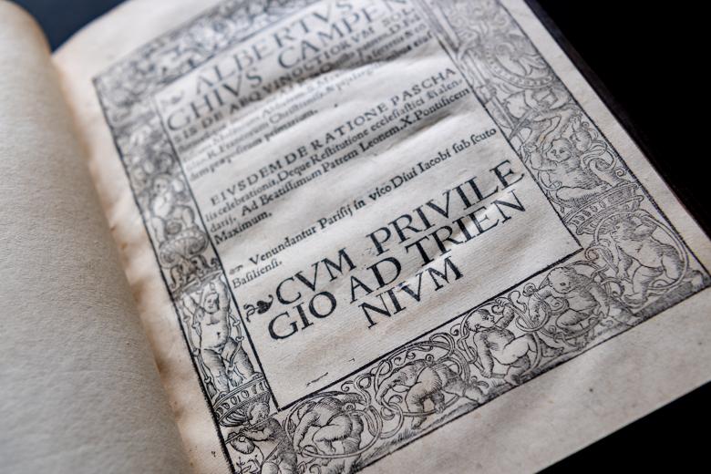 Detail of a printed books shows text in Latin on title page. Decorative frame includes babies.