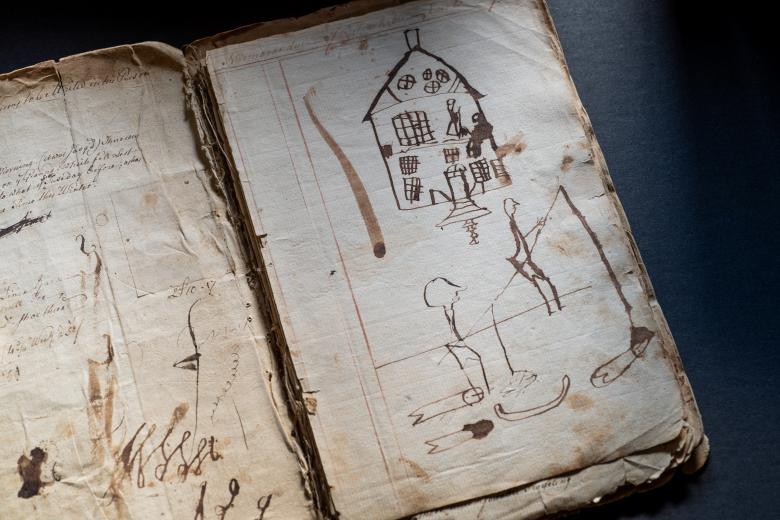 Detail of manuscript diary shows childlike drawings of a house and people fishing.