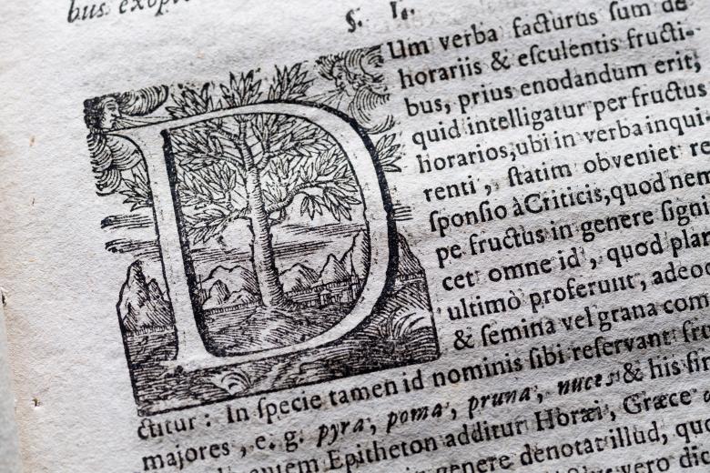 Detail of a printed book shows a page with text in Latin and elegant typography.