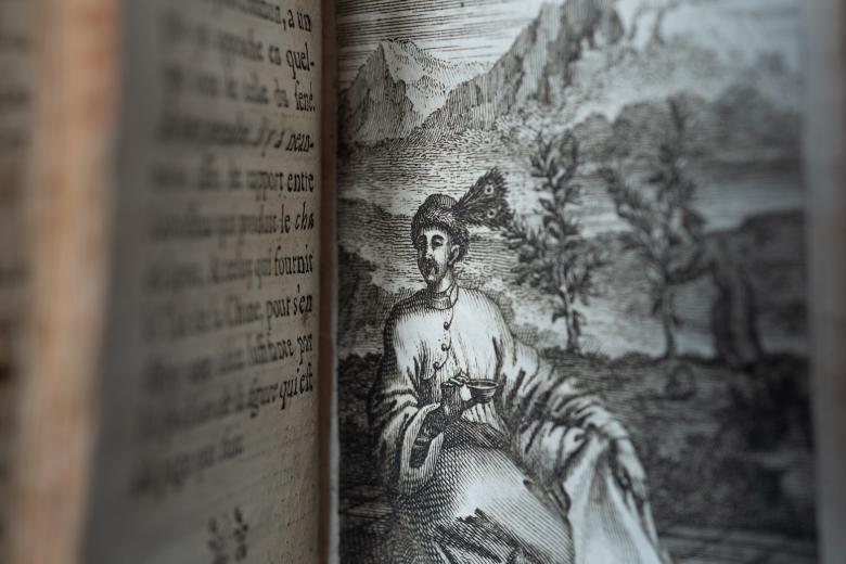 Detail of a printed text shows an illustration of a person in a turban sitting outdoors with mountainside visible and holding a cup.