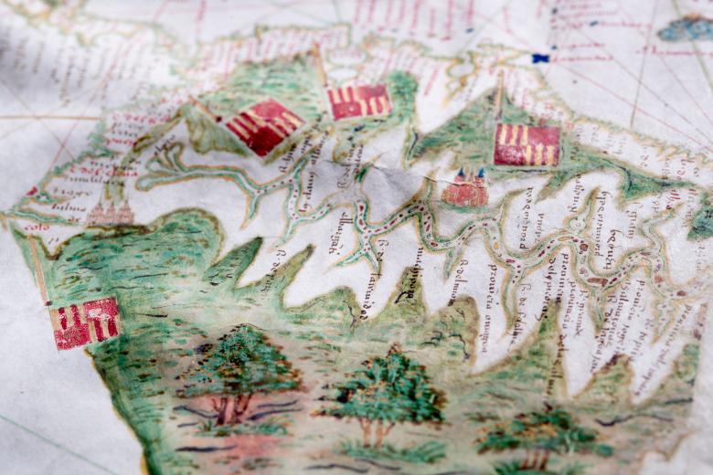 Detail of a hand colored manuscript map shows flags and trees along a coastal region.