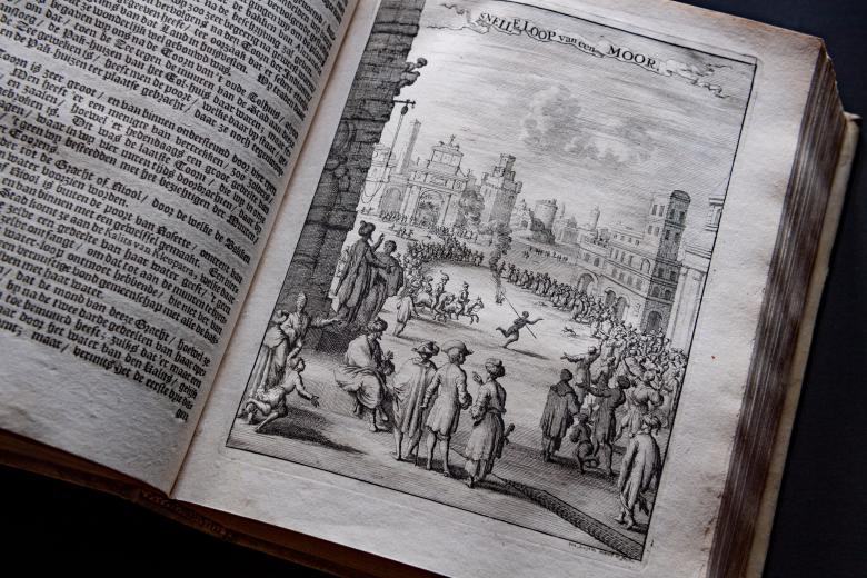 Detail of a printed book shows a full-page illustration of people standing in a town square with buildings surrounding them and in the background. Text in Dutch on the opposite page.