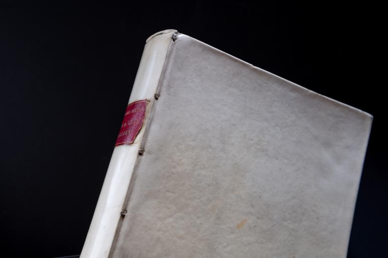 Detail of a printed book shows white binding and small red label on the spine.