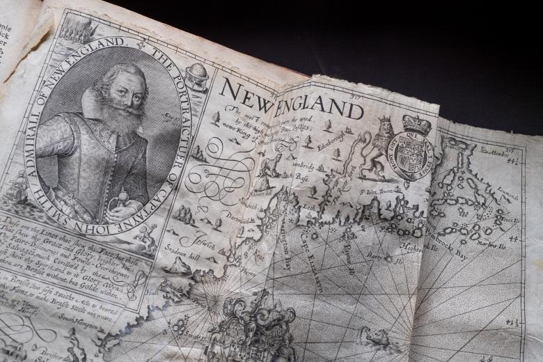 Detail of a printed fold-out map shows a portrait of a man, decorative cartouche, latitude and longitude lines, and text in English.
