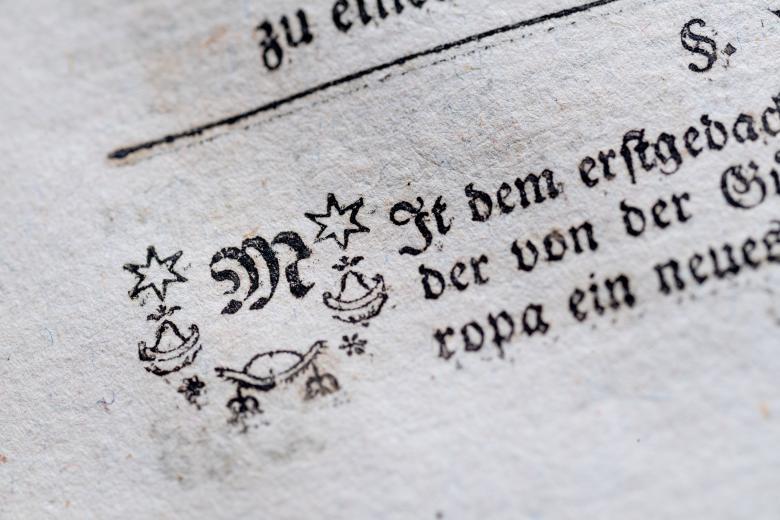 A printed text in German shows decorative elements (stars, flowers, etc) around the first letter of the page.