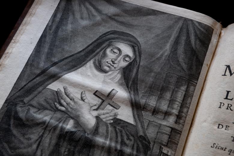 Detail of a printed book shows an illustration of a nun holding a cross to her chest.