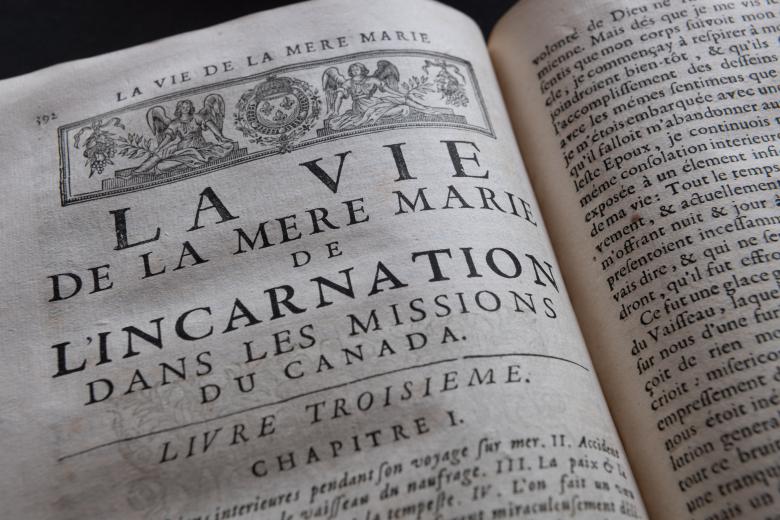 Detail of a printed book shows a decorative headpiece and text in French.
