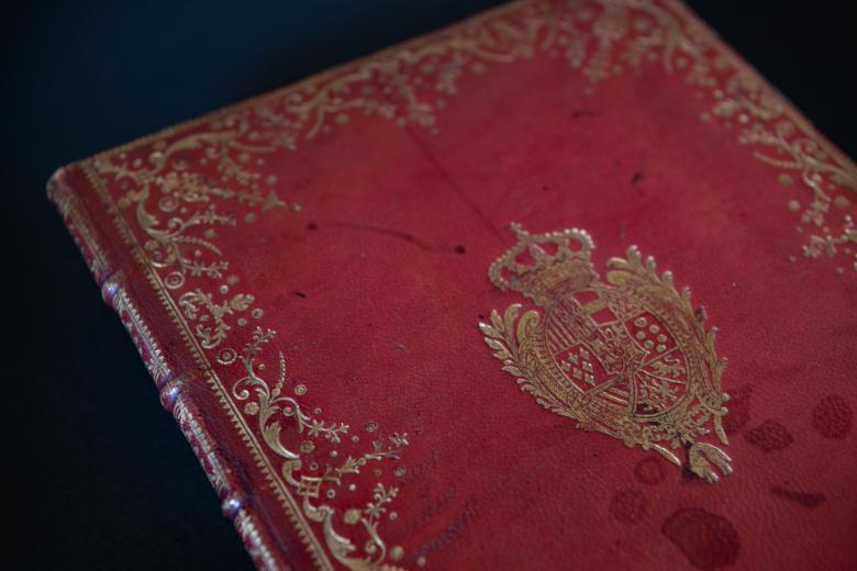 Detail of red morocco binding shows gold detail at the border and a coat of arms in the center.