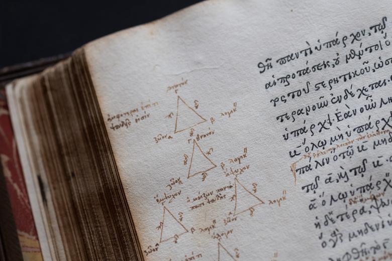 Detail of a printed text in Greek and manuscript notations of triangles and Greek text written in the margins.