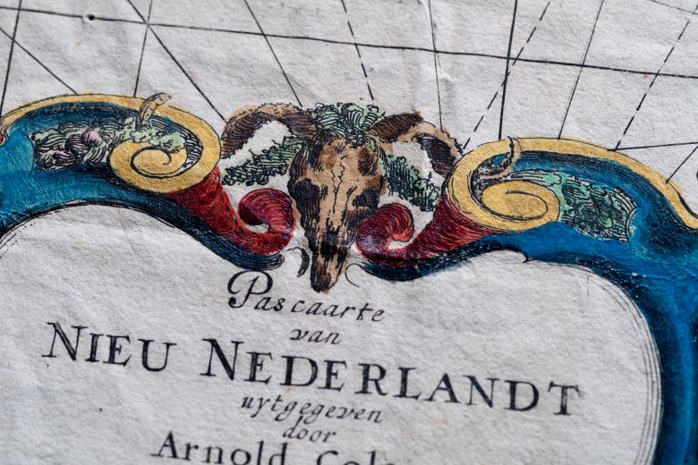 Detail of a colored engraved map shows decorative cartouche that includes the map title, drawings of ribbons, flowers, and an animal skull. 