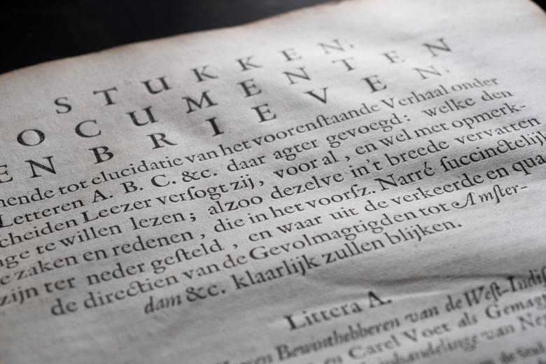 Detail of a printed book shows a page with text in Dutch.