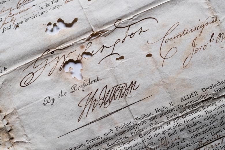 Detail from a weathered printed document, that includes manuscript inscriptions and autograph, shows text in Dutch from the president of the united states.