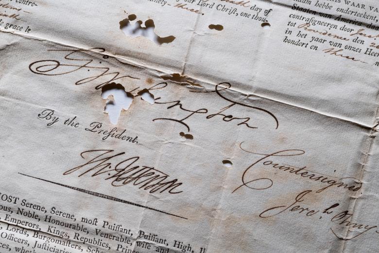 Detail from a weathered printed document, that includes manuscript inscriptions and autograph, shows text in Dutch from the president of the united states.