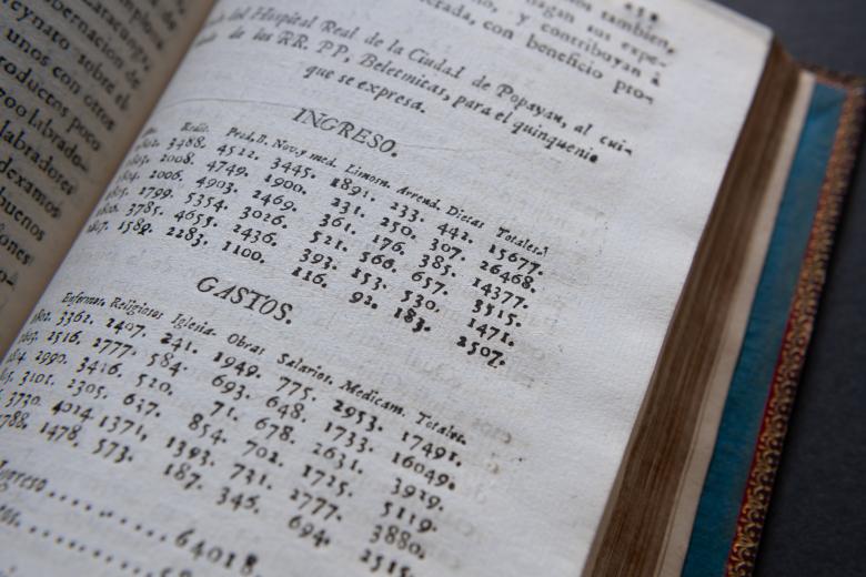 Detail from a printed book shows text in Spanish including "Ingreso" and "Gastos" and charts below those labels.