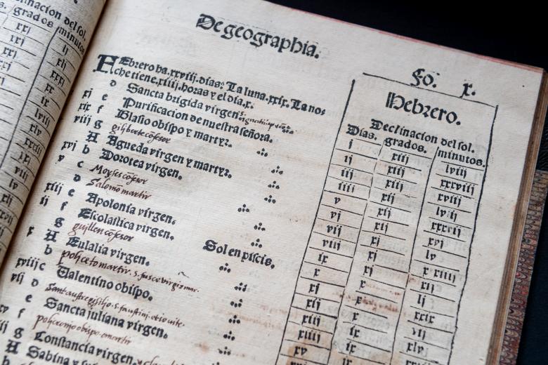 Detail of a printed book shows text in Spanish reading "De geographia" at the top and a list and chart below.