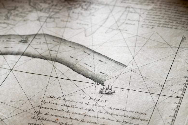 Detail of an engraved map shows a ship sailing, text in French, and lines of latitude and longitude.