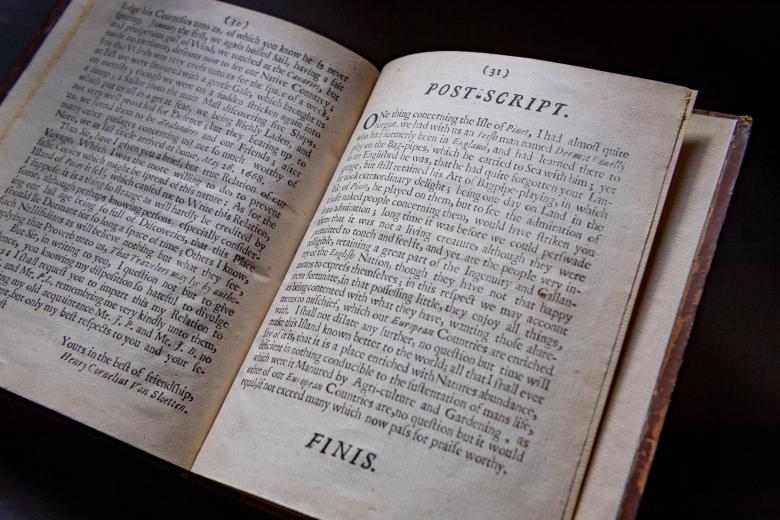 Detail of a printed book shows text in English. "Post Script" written at the top of the page and "Finis" written at the bottom.
