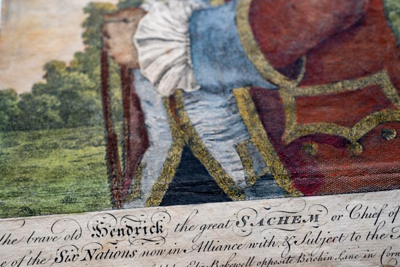 Detail of an engraved, hand colored print shows text in English and partial view of coat and hands.
