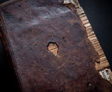 Detail from book cover shows dark brown binding with a missing piece in the front and worn sides.