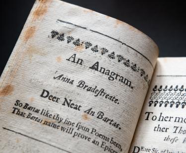 Detail of a printed book shows worn papers and header text reading "An Anagram. Anna Bradestreate" and other text in English.