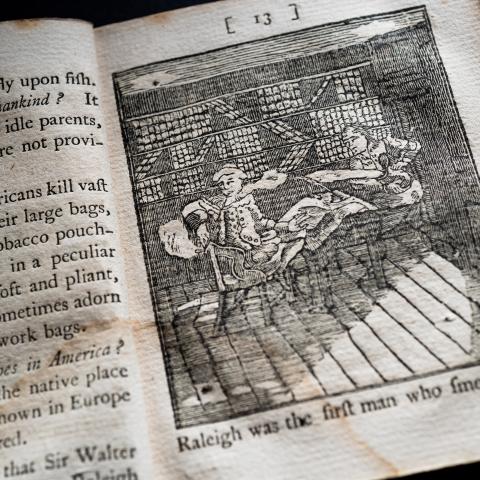 image of an opened book showing printed text on one page and an image of a man smoking tobacco on the opposite page